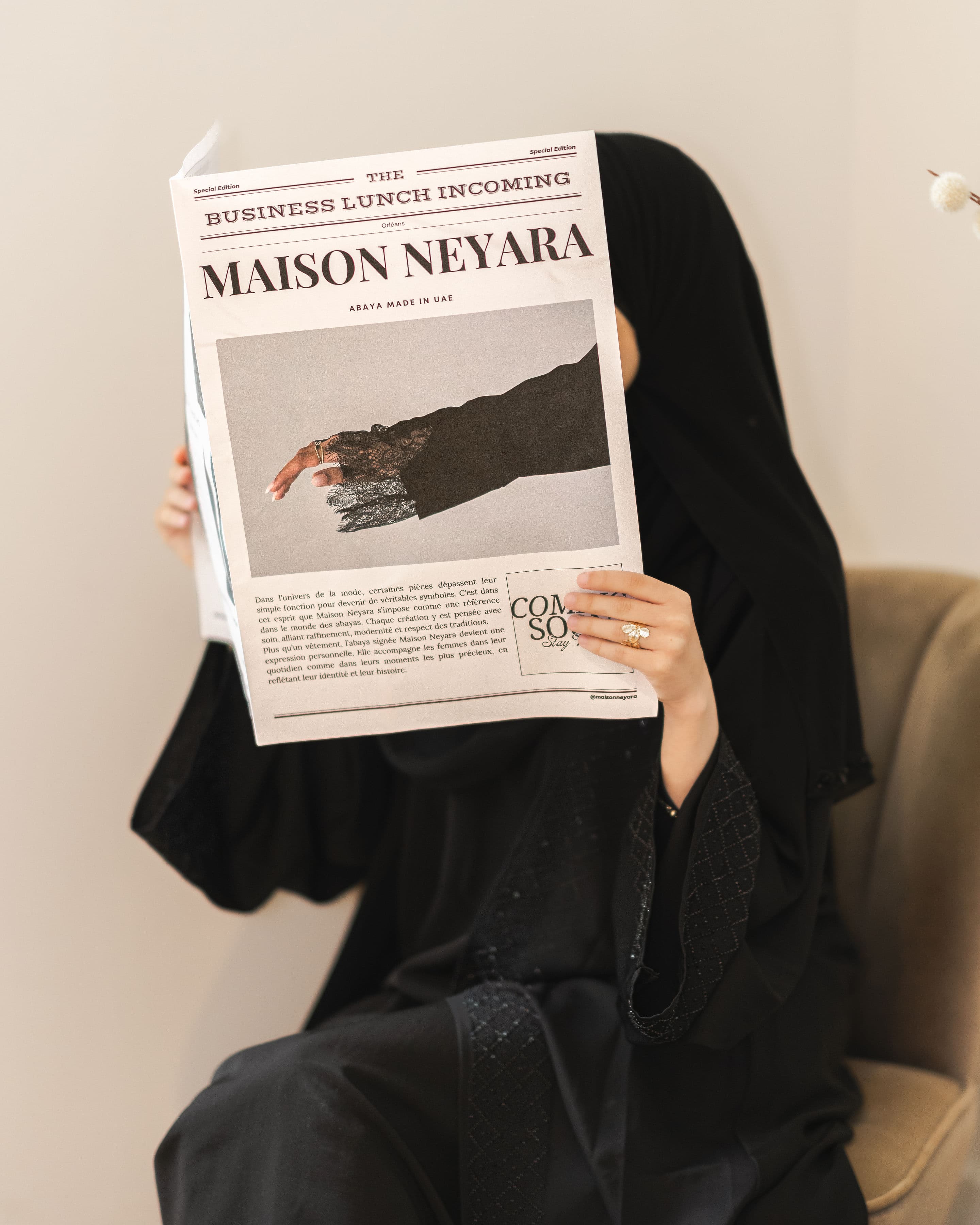 Femme en abaya noire tenant un journal Maison Neyara